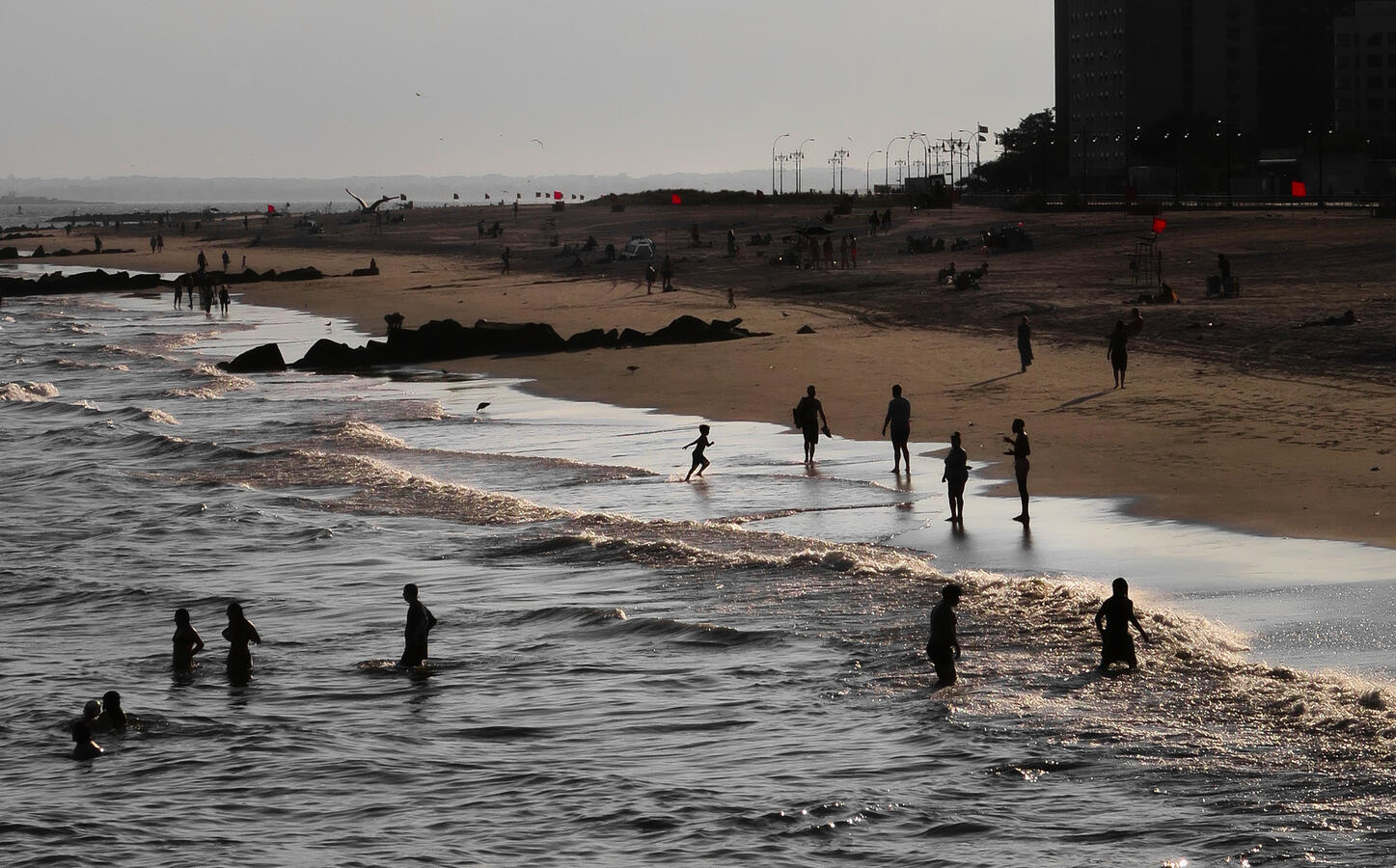 Silhouetted figures on Coney Island beach at sundown, with a running child centered in the image.